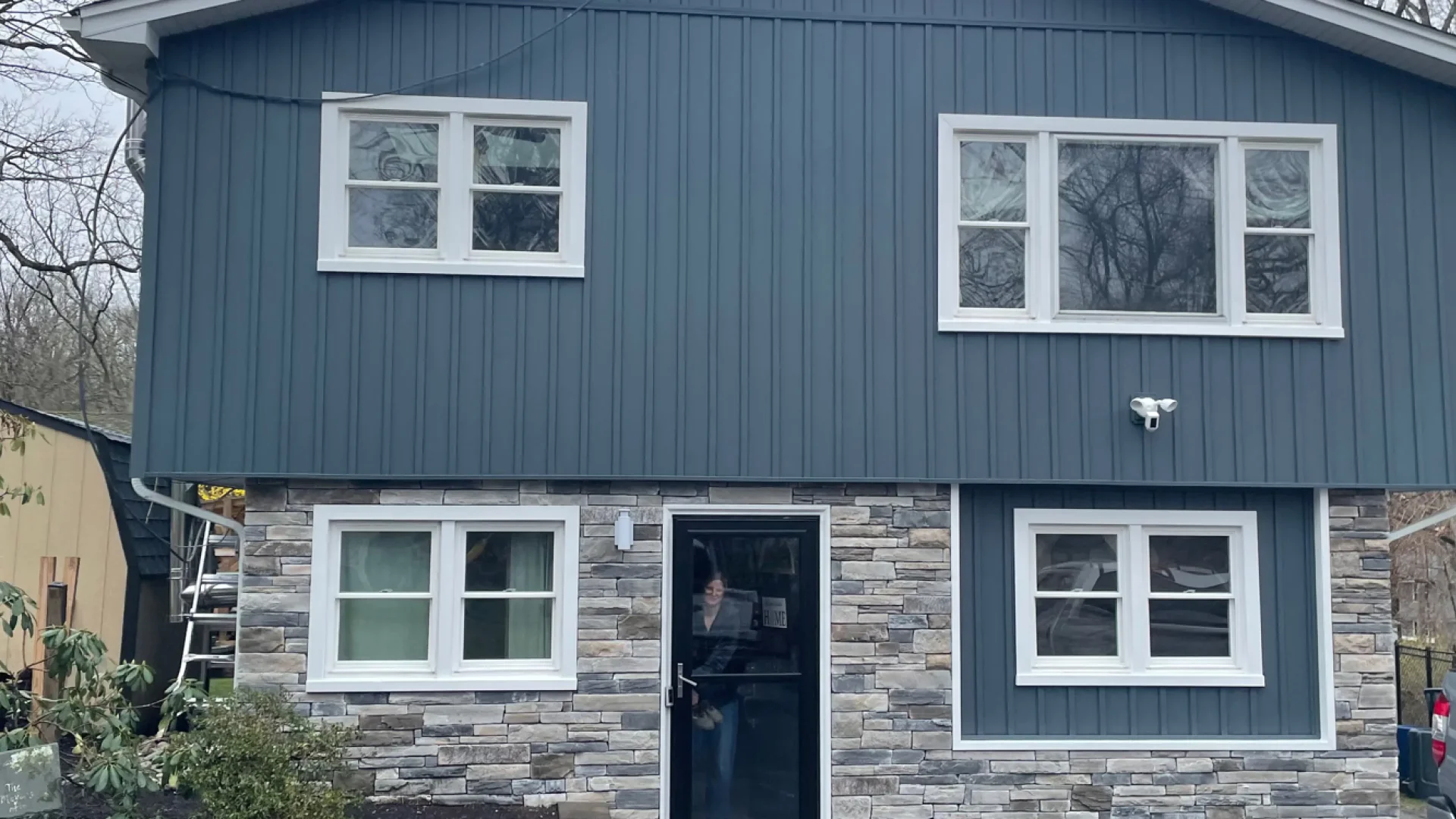 Modern home exterior featuring charcoal blue vertical siding and light gray stacked stone veneer entryway.
